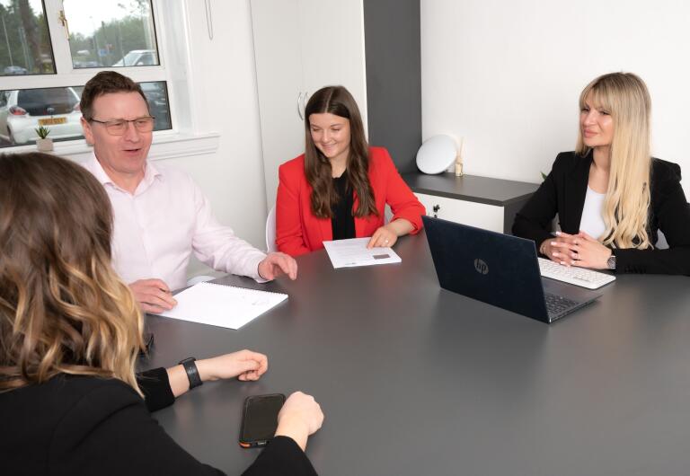 Scotia Financial team in a meeting. Four people at table: man in pink shirt, woman in red jacket, Viktorija Thain, and person facing away.